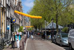 Amsterdam und Umgebung April 2025 Frühlingshafte Atmosphäre in einer belebten Amsterdamer Straße mit festlicher Dekoration Amsterdam und Umgebung April 2025 Straßenszene in Amsterdam mit orangefarbenen Luftballons und Passanten