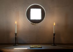 Amsterdam und Umgebung April 2025 Ein leuchtendes Quadrat an der Wand, flankiert von Kerzen auf einem Tisch Amsterdam und Umgebung April 2025 Kunstwerk mit leuchtendem Quadrat, zwei Kerzen und Buch auf Tisch