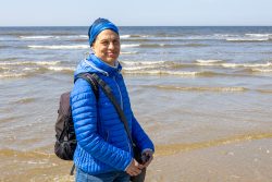 Amsterdam und Umgebung April 2025 Eine Frau genießt einen Tag am Strand mit blauem Himmel Amsterdam und Umgebung April 2025 Frau in blauer Jacke steht am Meer mit Wellen im Hintergrund