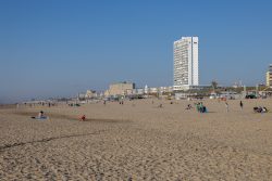 Amsterdam und Umgebung April 2025 Besucher entspannen sich am Strand von Scheveningen unter blauem Himmel Amsterdam und Umgebung April 2025 Strand von Scheveningen mit Hochhaus im Hintergrund, Besucher genießen sonniges Wetter