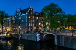 Amsterdam und Umgebung April 2025 Ein beleuchtetes Gebäude an einem Kanal in Amsterdam bei Nacht Amsterdam und Umgebung April 2025 Historische Architektur und Kanal in Amsterdam bei Nacht