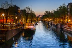 Amsterdam und Umgebung April 2025 Ein stimmungsvoller Blick auf Amsterdams beleuchtete Kanäle bei Sonnenuntergang Amsterdam und Umgebung April 2025 Beleuchteter Kanal in Amsterdam bei Sonnenuntergang mit Booten und Bäumen
