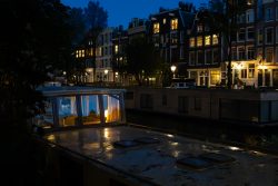 Amsterdam und Umgebung April 2025 Ein stimmungsvoll beleuchtetes Hausboot auf einem Kanal bei Dämmerung in Amsterdam Amsterdam und Umgebung April 2025 Hausboot leuchtet warm auf einem Amsterdamer Kanal bei Nacht