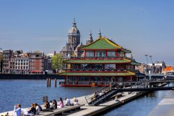 Amsterdam und Umgebung April 2025 Das schwimmende Restaurant vor der Amsterdamer Skyline und der historischen Kirche Amsterdam und Umgebung April 2025 Chinesisches Restaurant auf Wasser vor der Kirche in Amsterdam