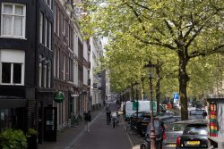 Amsterdam und Umgebung April 2025 Ein sonniger Tag in Amsterdam mit Fahrradfahrern und historischen Gebäuden Amsterdam und Umgebung April 2025 Malersiche Amsterdamer Straße mit Fahrrädern und Ziegelgebäuden an einem sonnigen Tag