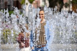 Amsterdam und Umgebung April 2025 Eine Frau blickt durch einen lebhaften Springbrunnen mitten in der Stadt Amsterdam und Umgebung April 2025 Frau steht hinter einem sprudelnden Springbrunnen im Freien