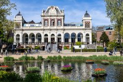 Amsterdam und Umgebung April 2025 Das beeindruckende Gebäude im Vondelpark zeichnet sich durch seine elegante Architektur aus. Amsterdam und Umgebung April 2025 Historisches Gebäude im Vondelpark Amsterdam vor einem Teich mit Blumeninseln