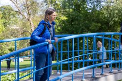 Amsterdam und Umgebung April 2025 Eine Frau genießt den sonnigen Tag auf einer blauen Brücke Amsterdam und Umgebung April 2025 Frau in blauer Jacke auf einer blauen Brücke in einem grünen Park