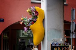 Amsterdam und Umgebung April 2025 Ein gelber Klompen voller Blumen schmückt eine lebhafte Straßenecke Amsterdam und Umgebung April 2025 Gelber Klompen mit bunten Blumen an einer Hauswand in einer belebten Gasse