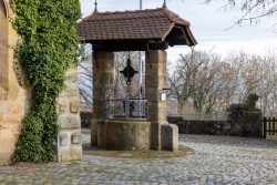 Bamberg - Bamberg Weihnachtsmarkt 2023 Ein historischer Brunnen mit einem hölzernen Dach, umgeben von Bäumen und Kopfsteinpflaster Bamberg - Bamberg Weihnachtsmarkt 2023 Historischer Steinbrunnen mit Dach auf gepflastertem Platz