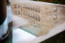 Frankfurt IG Farbengebaeude Goethe Universitaet Spiegelung eines Gebäudes mit Steinmauer und Fenstern im Regenwasser auf dem Bürgersteig