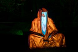 Frankfurt Palmengarten Winterlichter 2025 Leuchtende Skulptur einer sitzenden Figur mit Kapuze bei Nacht