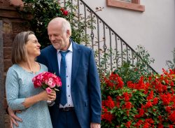 Hochzeitsfotografie Lächelndes älteres Paar mit Blumenstrauß vor rotem Blumenbeet