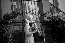 Hochzeitsfotografie Älteres Paar in Schwarz-Weiß vor Gebäude, das sich liebevoll küsst