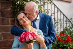 Hochzeitsfotografie Älteres Paar umarmt sich im Garten, Mann hält Frau mit Blumenstrauß