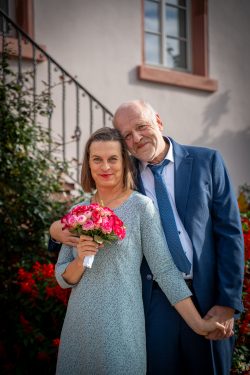 Hochzeitsfotografie Älteres Paar hält Blumenstrauß vor Haus in der Sonne