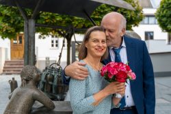 Hochzeitsfotografie Älteres Paar posiert liebevoll mit Blumenstrauß an einem Brunnen