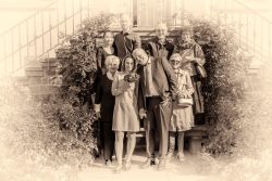 Hochzeitsfotografie Sepia Hochzeitsporträt von acht Personen vor einem mit Blumen umrahmten Eingang