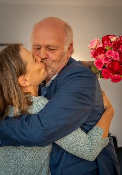 Hochzeitsfotografie Älteres Paar umarmt sich und küsst leidenschaftlich mit Blumenstrauß