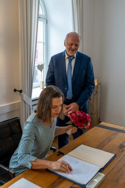 Hochzeitsfotografie Frau unterschreibt Dokument, während Mann mit Blumenstrauß daneben steht