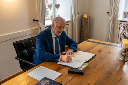 Hochzeitsfotografie Ein Mann im Anzug unterschreibt ein Dokument an einem Holztisch