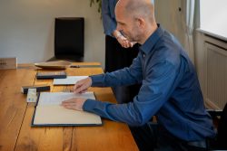 Hochzeitsfotografie Mann unterschreibt Dokumente an einem hölzernen Tisch in einem Büro