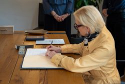 Hochzeitsfotografie Ältere Frau unterschreibt Dokument auf Holztisch, nebeneinander Bücher und Personen im Hintergrund