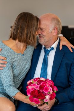 Hochzeitsfotografie Älteres Paar umarmt sich mit Blumenstrauß und formeller Kleidung