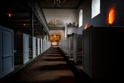 Insel Sylt Februar 2025 Ein ruhiger Moment in einer historischen Kirche mit beleuchtetem Altar Insel Sylt Februar 2025 Historische Kirche mit leeren Holzbanken und beleuchtetem Altar