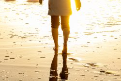 Insel Sylt Februar 2025 Ein friedlicher Moment am Strand bei Sonnenuntergang Insel Sylt Februar 2025 Person im Mantel geht barfuß am sonnigen Strand entlang