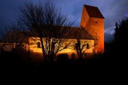 Insel Sylt Februar 2025 Eine stimmungsvoll beleuchtete Kirche hebt sich gegen den dramatisch bewölkten Nachthimmel ab Insel Sylt Februar 2025 Beleuchtete alte Kirche bei Nacht mit dramatischem Himmel und Bäumen