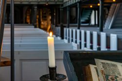 Insel Sylt Februar 2025 Einzelne Kerze erleuchtet historische Kirchenbänke Insel Sylt Februar 2025 Kerze in historischer Kirche mit alten Büchern im Vordergrund