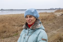 Insel Sylt Februar 2025 Eine Frau genießt einen kalten Wintertag am Seeufer Insel Sylt Februar 2025 Frau in blauem Mantel und Mütze steht lächelnd in einer winterlichen Landschaft am See
