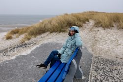 Insel Sylt Februar 2025 Eine Frau genießt den kühlen Tag am Strand zwischen den Dünen Insel Sylt Februar 2025 Frau in blauer Jacke auf Bank an windigem Strand mit Dünen