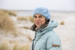 Insel Sylt Februar 2025 Eine Frau genießt einen Spaziergang am ruhigen Strand. Insel Sylt Februar 2025 Frau im blauen Mantel und Mütze an einem Strand an einem bewölkten Tag