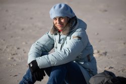 Insel Sylt Februar 2025 Eine Frau genießt einen kühlen Tag am Strand in warmer Kleidung Insel Sylt Februar 2025 Frau in blauer Jacke und Mütze sitzt am Strand