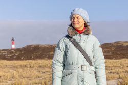 Insel Sylt Februar 2025 Eine Frau genießt einen sonnigen Tag auf Sylt vor einem Leuchtturm Insel Sylt Februar 2025 Frau in Wintermantel vor Dünenlandschaft mit Leuchtturm auf Sylt