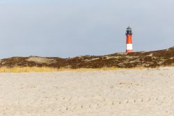 Insel Sylt Februar 2025 Ein Leuchtturm steht einsam auf einer sandigen Düne unter einem bewölkten Himmel. Insel Sylt Februar 2025 Leuchtturm auf sandiger Düne bei bewölktem Himmel