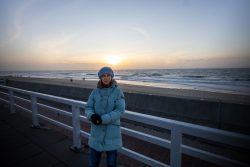 Insel Sylt Februar 2025 Eine Frau genießt den Sonnenuntergang am Meer Insel Sylt Februar 2025 Frau im blauen Mantel steht bei Sonnenuntergang am Strand