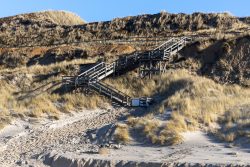 Insel Sylt Februar 2025 Holztreppe führt durch die Dünen an der Nordseeküste Insel Sylt Februar 2025 Holztreppe in Dünenlandschaft an der Nordseeküste bei Sonnenschein