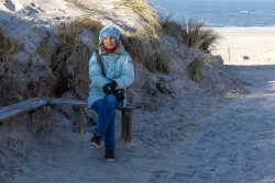 Insel Sylt Februar 2025 Eine Frau genießt die Ruhe am Strand mit Blick auf das Meer Insel Sylt Februar 2025 Frau sitzt auf Bank am Strand, Sanddünen im Hintergrund