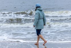 Insel Sylt Februar 2025 Eine Person genießt einen Spaziergang am kalten Strand. Insel Sylt Februar 2025 Person in blauer Jacke spaziert barfuß am winterlichen Strand