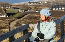 Insel Sylt Februar 2025 Eine Frau genießt die Wintersonne entlang der norddeutschen Küstenlandschaft Insel Sylt Februar 2025 Frau auf Holzzaun in norddeutscher Küstenlandschaft mit Dünen und Reetdachhäusern