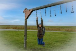 Insel Sylt und Hallig Hooge Oktober 2025 Eine Frau genießt einen Tag im Freien an einem Klettergerüst Insel Sylt und Hallig Hooge Oktober 2025 Frau hängt lächelnd an einem Outdoor-Klettergerüst unter blauem Himmel