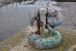 Insel Sylt und Hallig Hooge Oktober 2025 Eine farbenfrohe Holzskulptur zeigt eine kauernde Gestalt am Wasser. Insel Sylt und Hallig Hooge Oktober 2025 Bunte Holzskulptur einer kauernden Figur an einer Küste