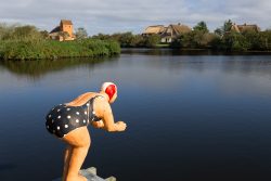 Insel Sylt und Hallig Hooge Oktober 2025 Eine Holzstatue eines Tauchers steht am Ufer eines ruhigen Sees vor malerischer Kulisse Insel Sylt und Hallig Hooge Oktober 2025 Holzstatue eines Tauchers am See mit strohgedeckten Häusern im Hintergrund