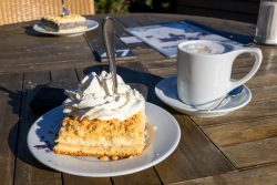 Insel Sylt und Hallig Hooge Oktober 2025 Ein köstlicher Käsekuchen mit frischer Sahne neben einer Tasse Kaffee Insel Sylt und Hallig Hooge Oktober 2025 Stück Käsekuchen mit Sahne und Kaffee auf einem Holztisch