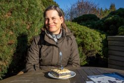 Insel Sylt und Hallig Hooge Oktober 2025 Eine Frau genießt ein sonniges Herbstnachmittag mit Kuchen im Freien Insel Sylt und Hallig Hooge Oktober 2025 Frau sitzt lächelnd im Freien bei Sonnenschein mit Kuchen