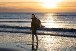 Insel Sylt und Hallig Hooge Oktober 2025 Eine Person genießt den Strand bei Sonnenuntergang, während sie im Wasser watet. Insel Sylt und Hallig Hooge Oktober 2025 Person am Strand bei Sonnenuntergang mit Rucksack