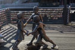 Lüneburg August 2024 Bronzestatue von drei spielenden Kindern vor einem Geländer mit Liebesschlössern
